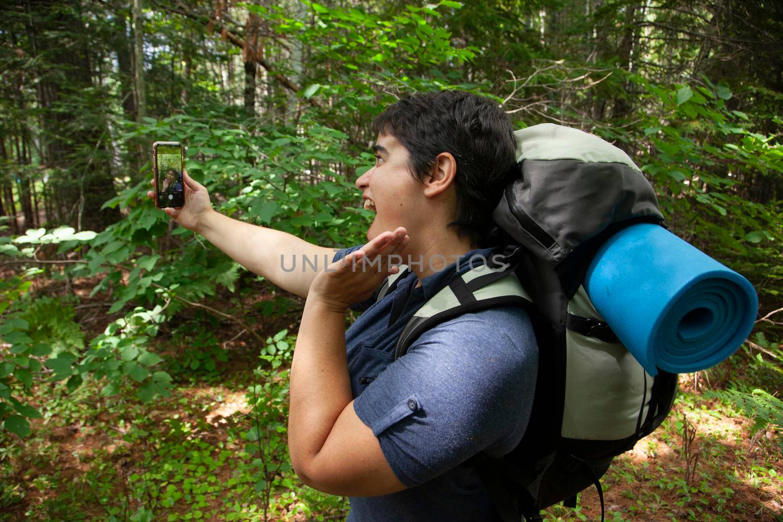 person posing vainly for a self portrait outside in nature with their cell phone 