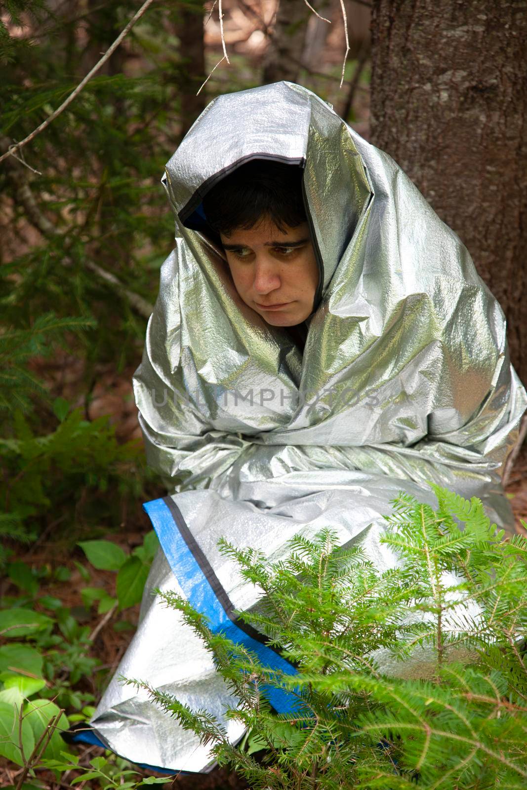  person wrapped in a tinfoil blanket looks scared, cold and lost in the woods 