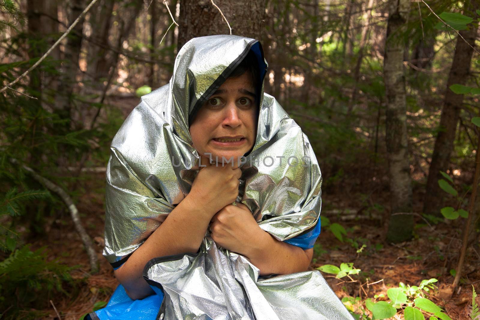 person wearing a space blanket in the woods to keep warm while they are lost makes an afraid expression 
