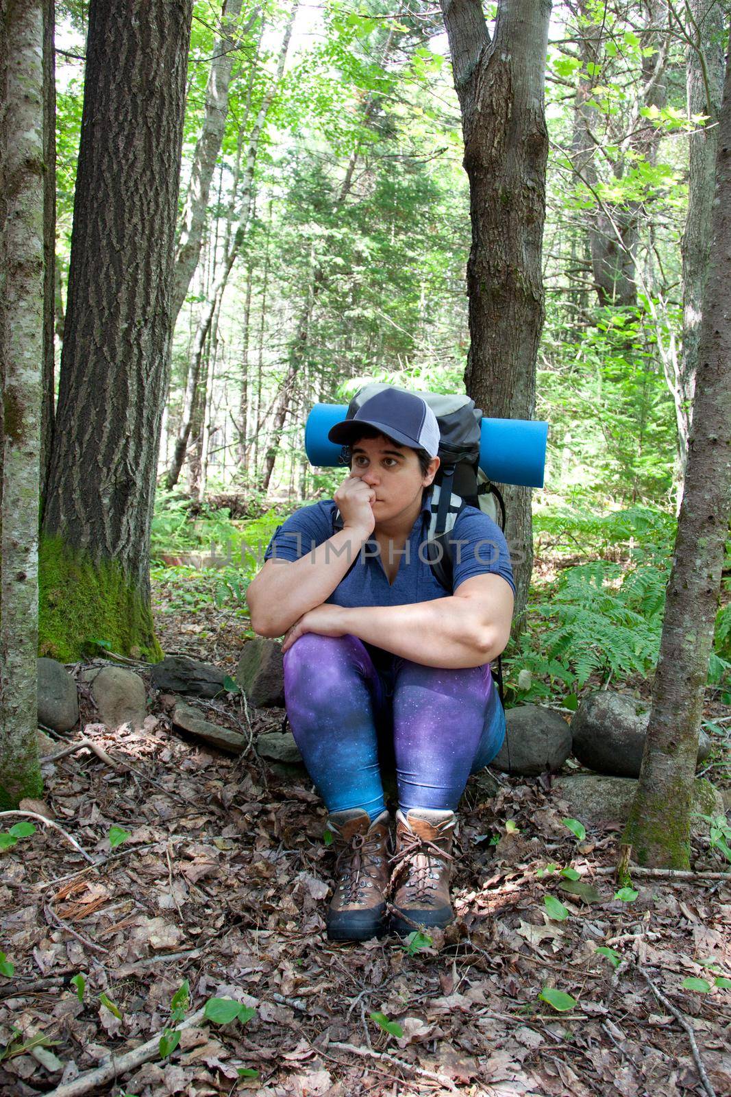 A hiker has become lost or anxious while hiking in the woods with a backpack and camping roll 