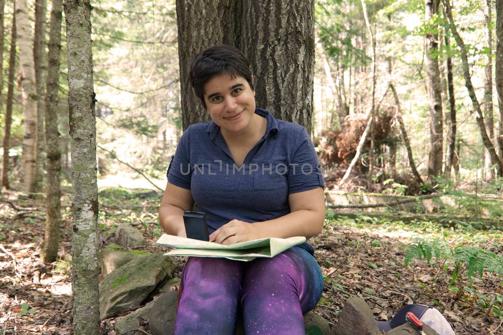 Adventurous woman with her map and compass smiles in the forest