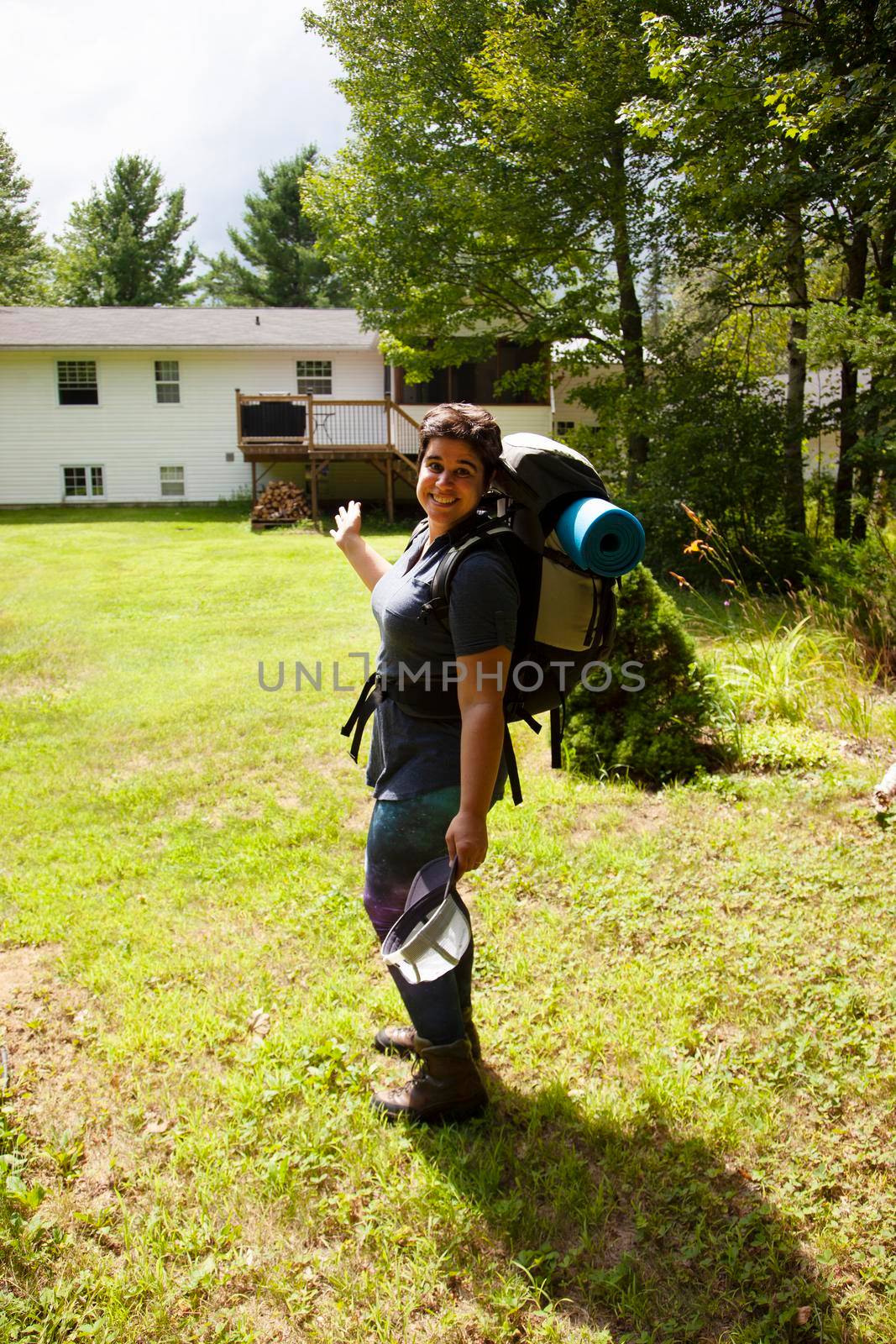  woman with a backpack and camp roll heading away from her house into the woods for adventure 