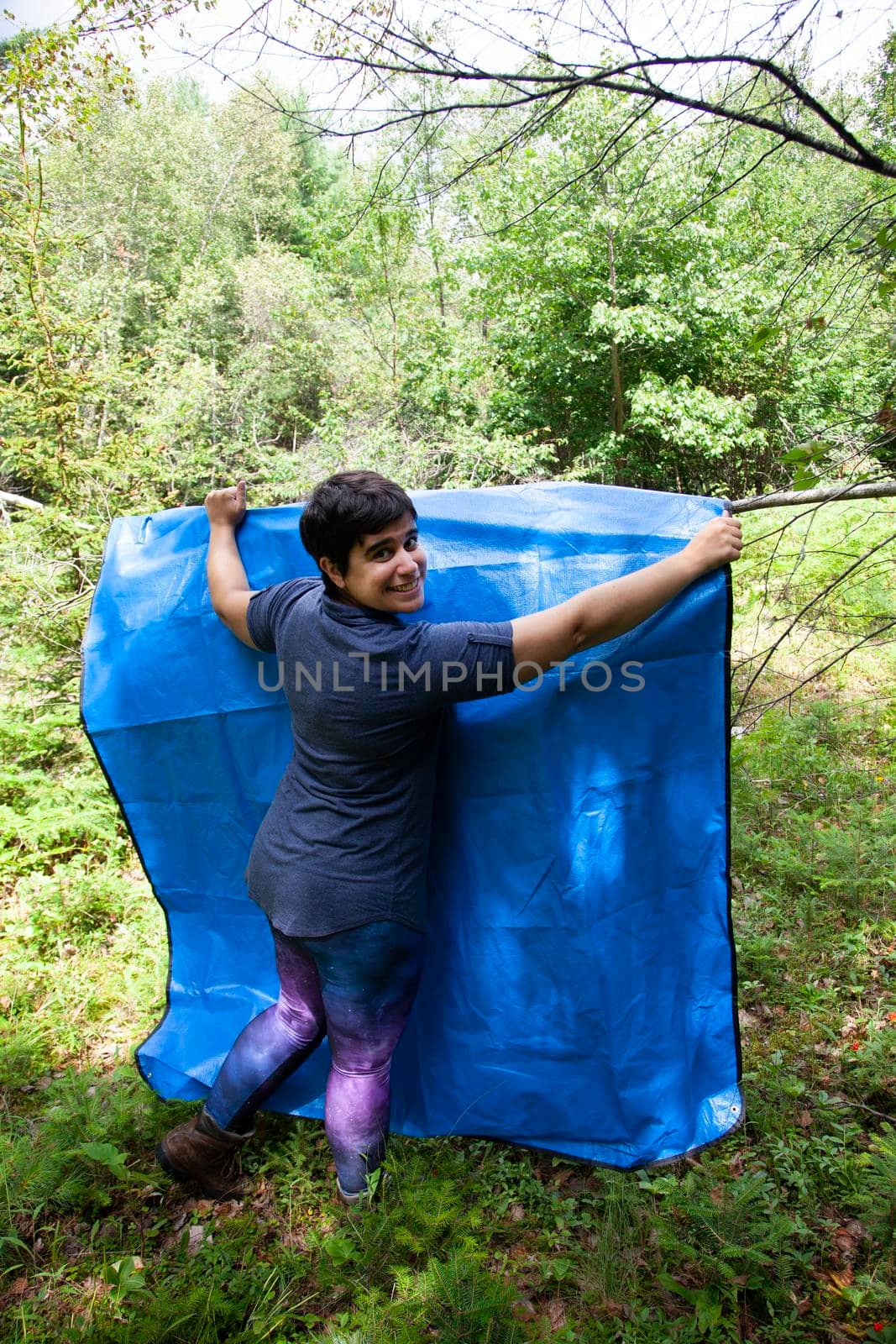  person camping or outdoors hangs up a blue tarp to dry in the sun 