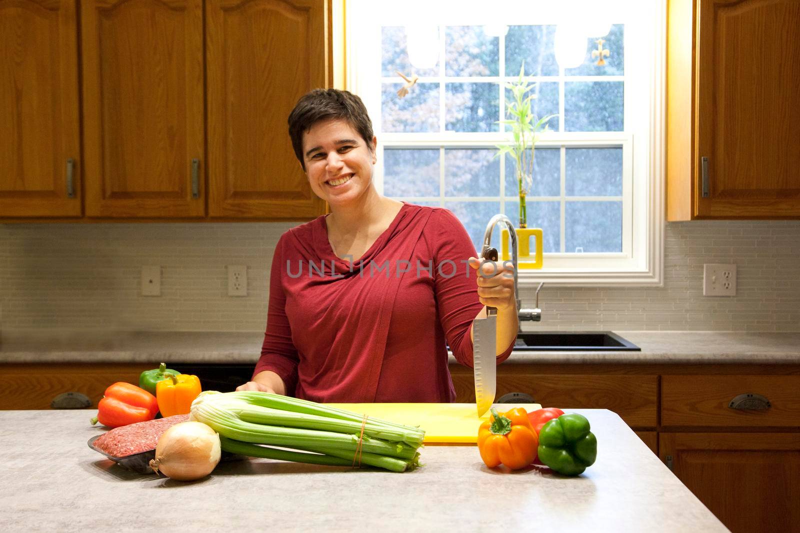 A smiling woman holds a cutting knife in her beautiful home kitchen ready to slice vegetables