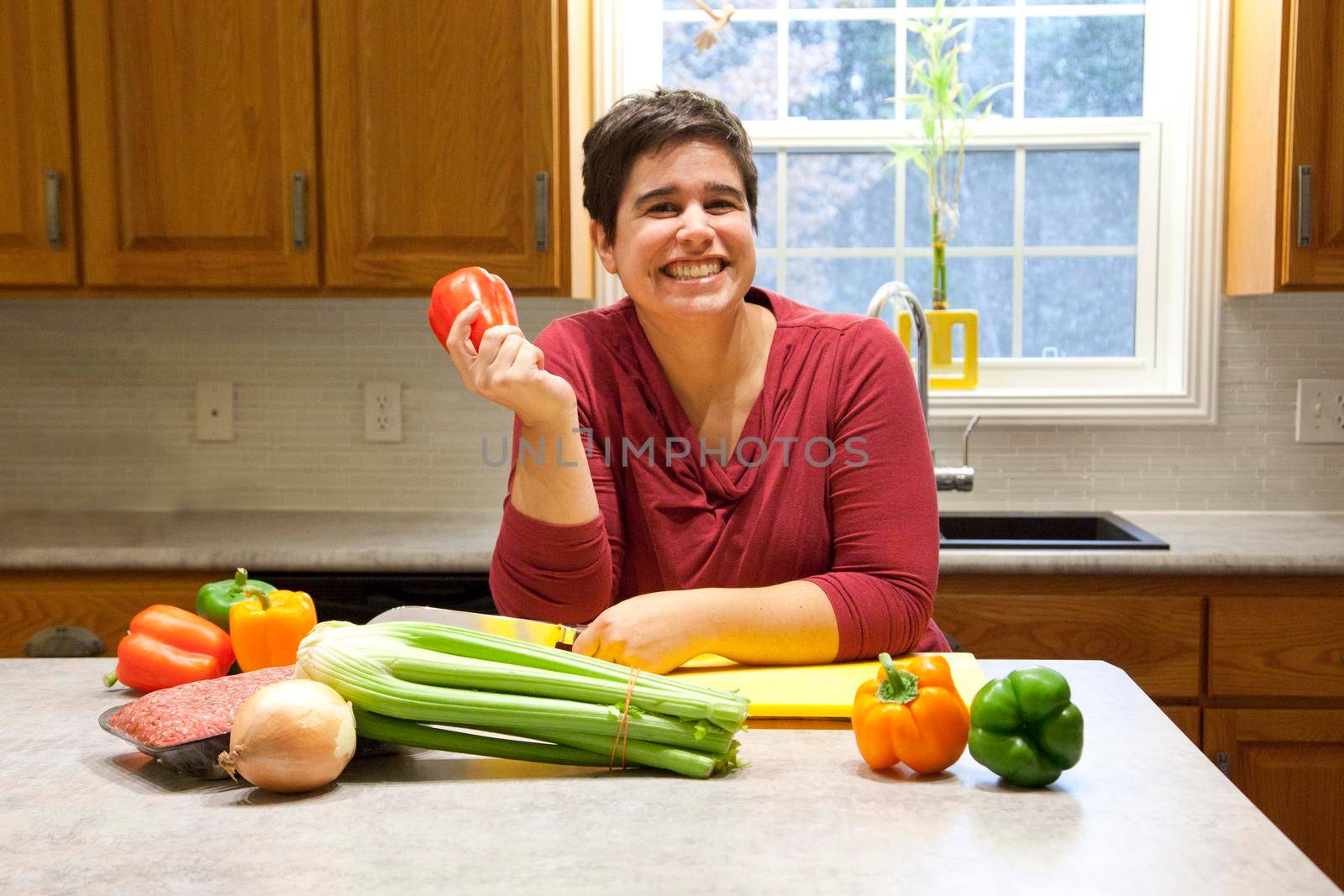 Holding a bell pepper and grinning in her beautiful kitchen, a woman prepares to cook healthy 