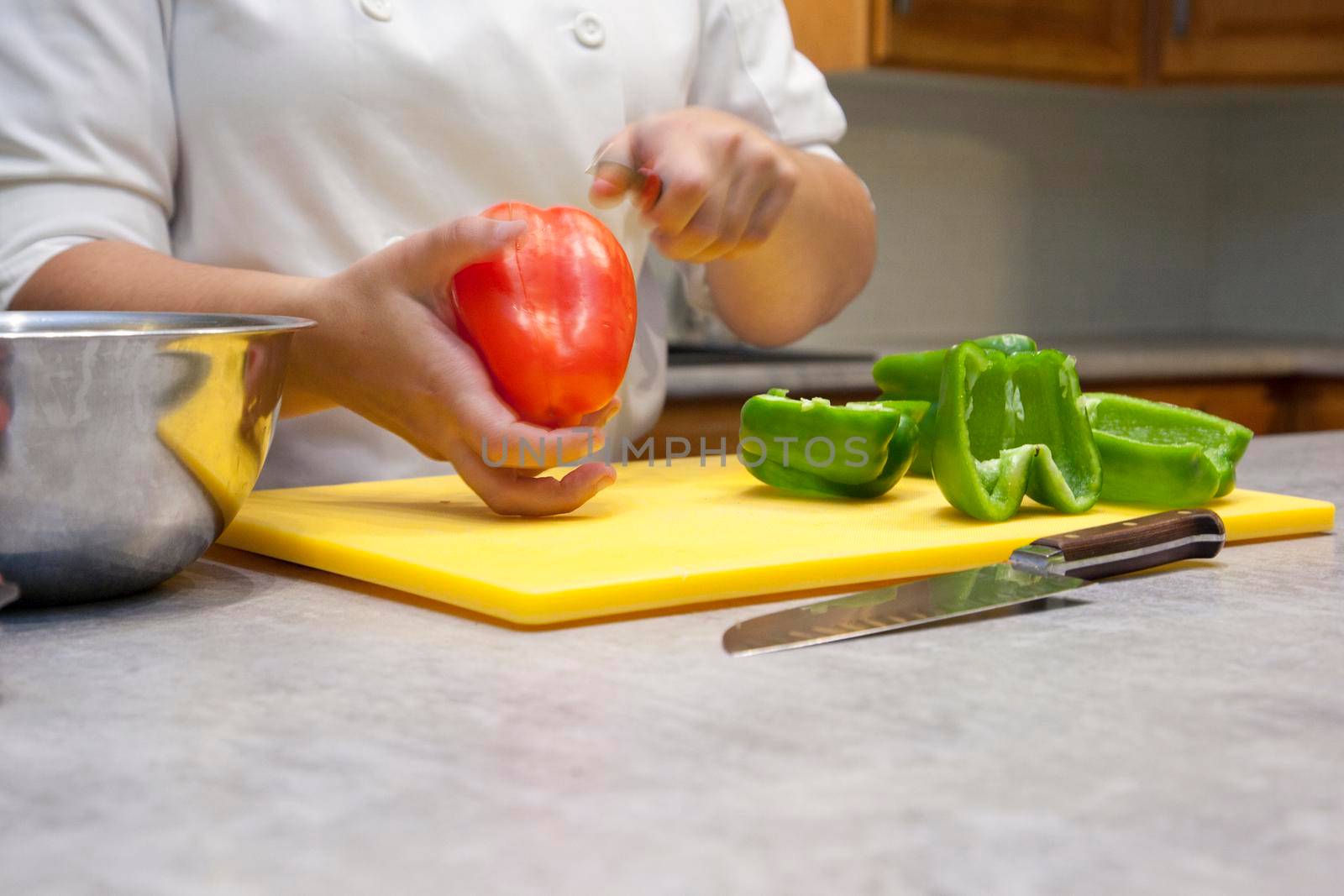 Close up of hands slicing a red bell pepper on a cutting board in the kitchen 