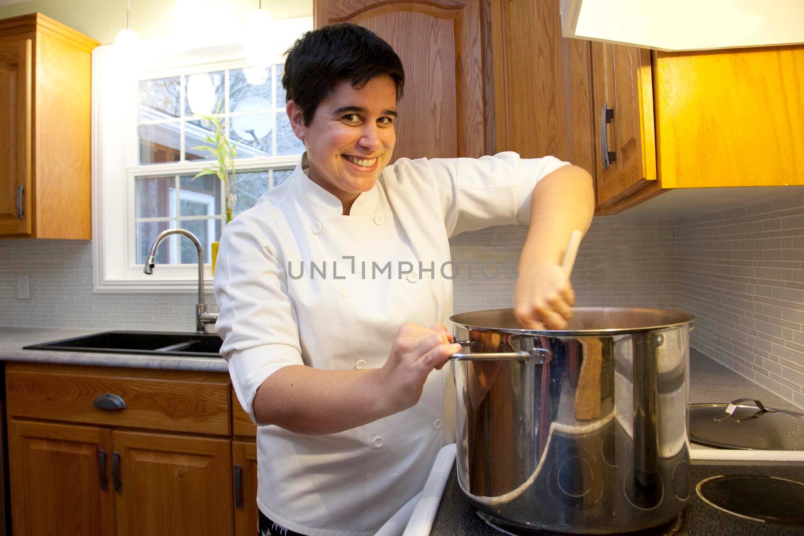  Person in a chef jacket stirs a huge vat of soup or stew with a wooden spoon over the stove 