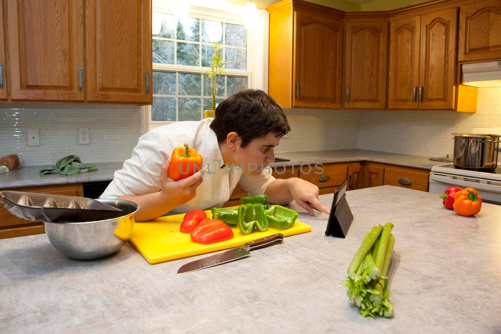 Chef in the kitchen holds a bell pepper and double checks ingredients or instructions on their tablet