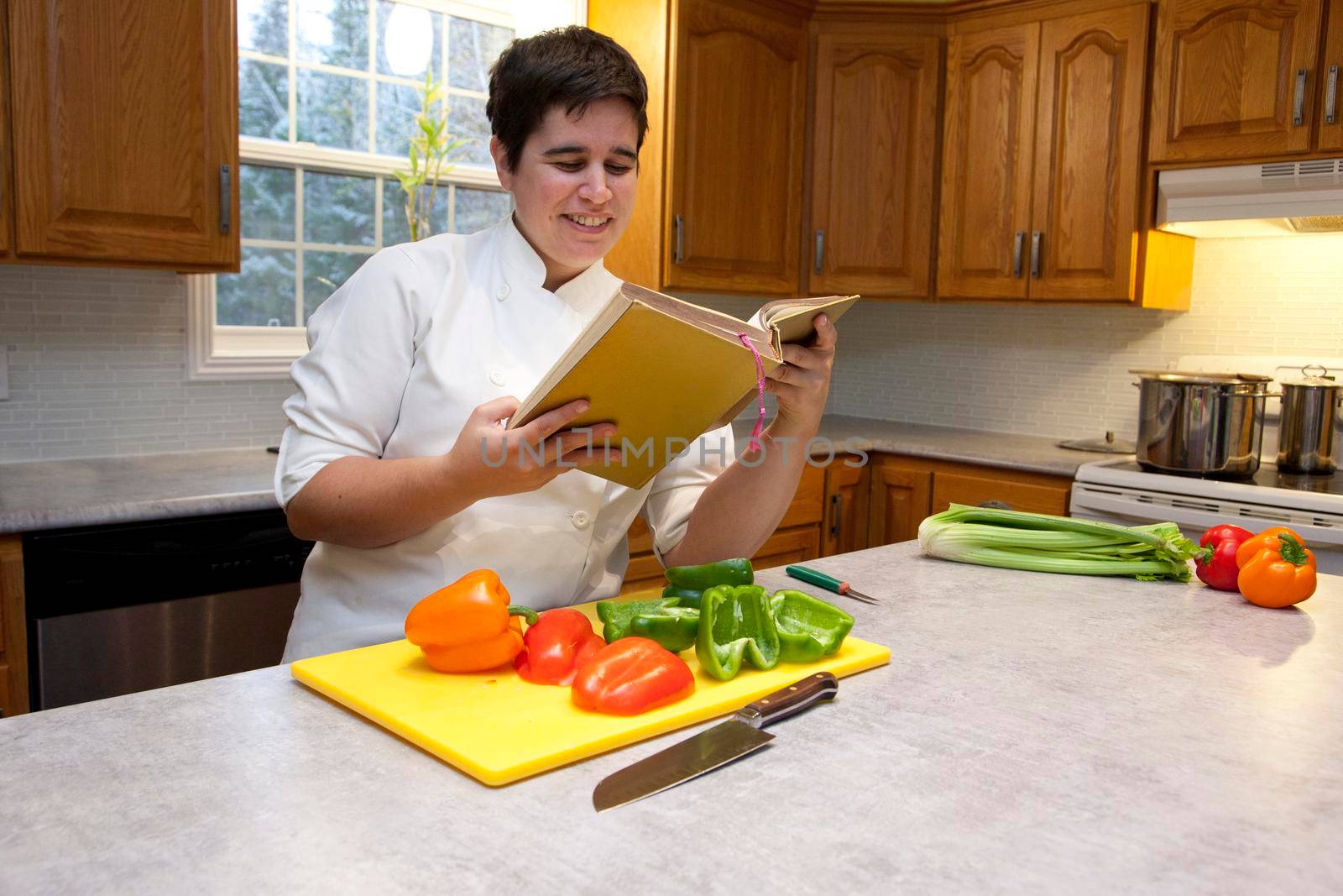 Woman in a chef's outfit in their kitchen with cut peppers smiles as they decide on a recipe