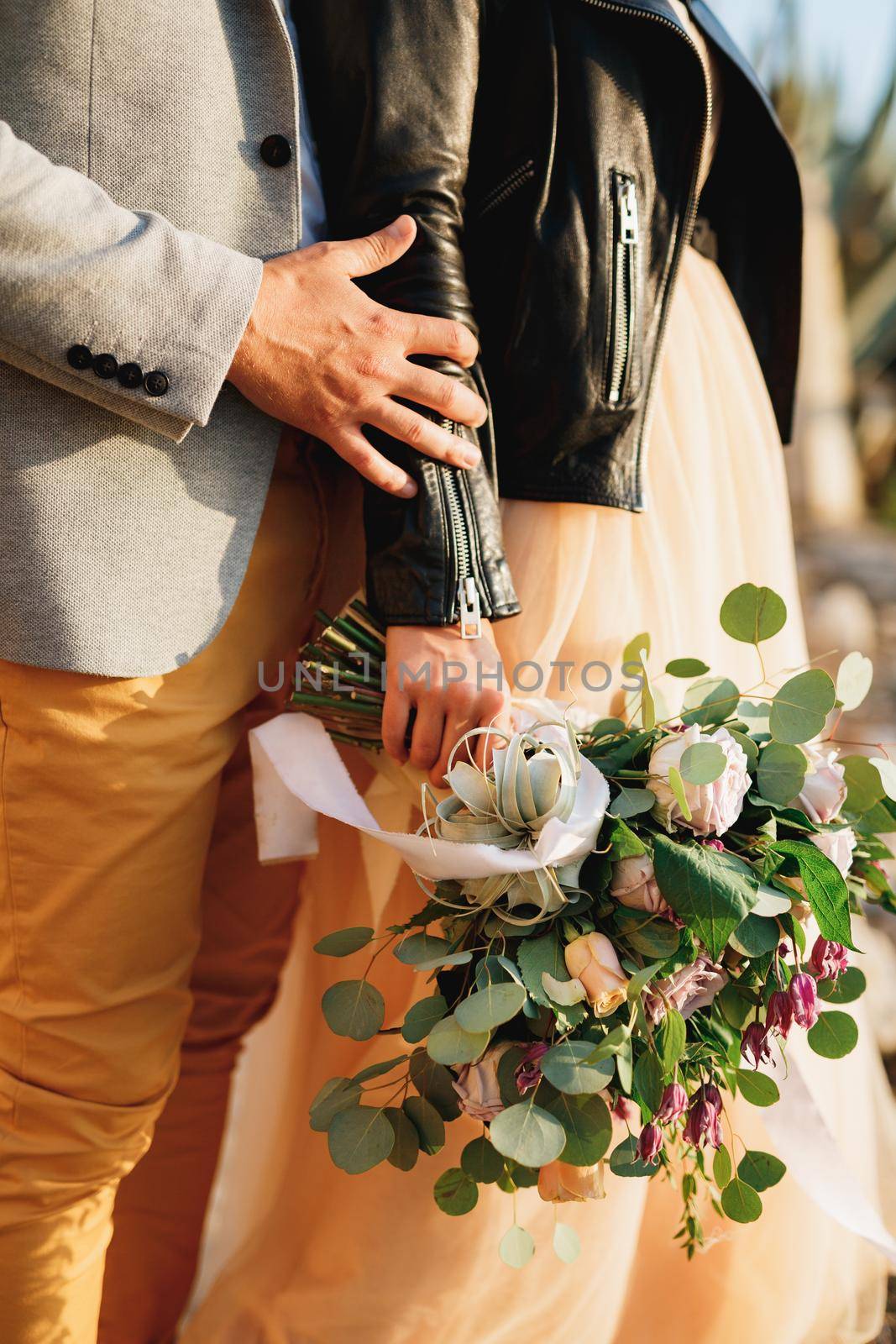 Groom holds bride's hand with a bouquet of flowers. Close-up of hands by Nadtochiy