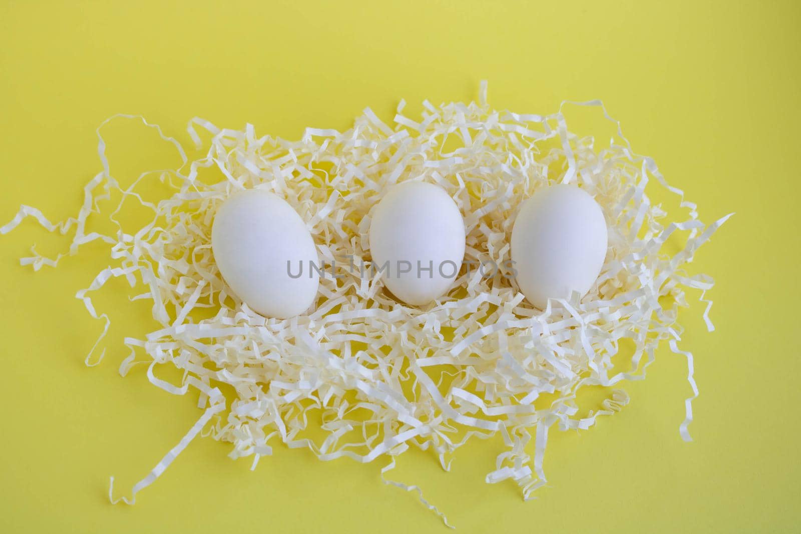 Three white eggs in tinsel on a yellow background. Easter Concept.
