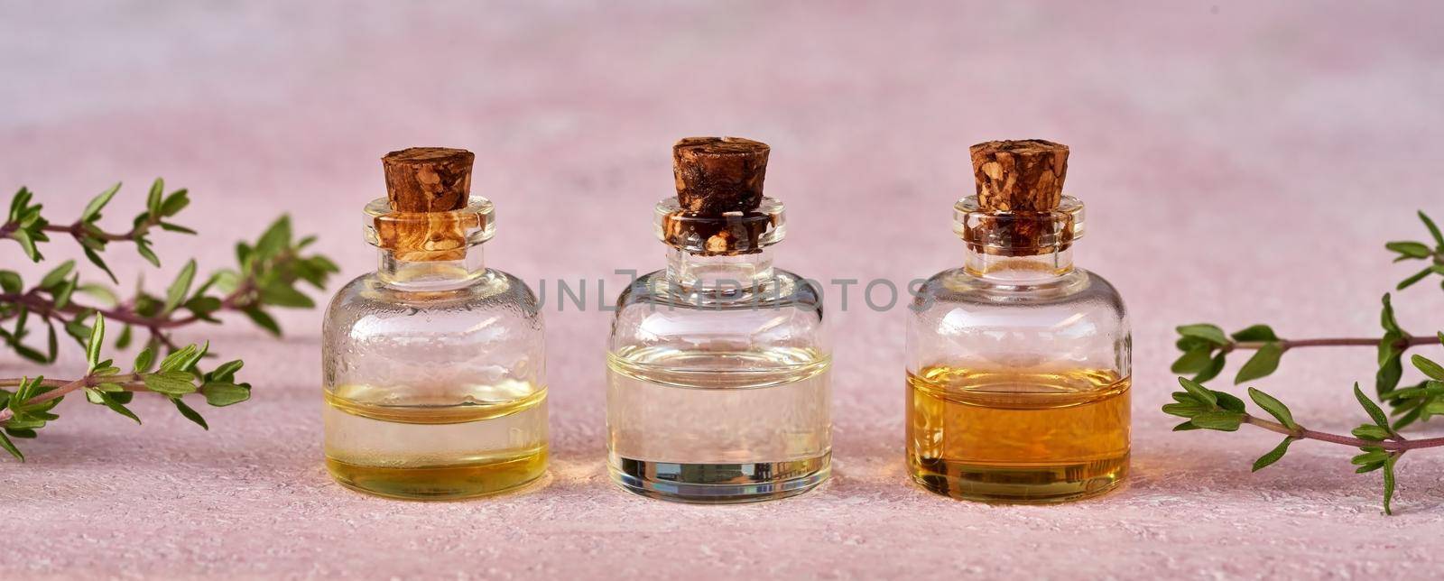 Essential oil bottles with fresh thyme twigs on pastel pink background by madeleine_steinbach