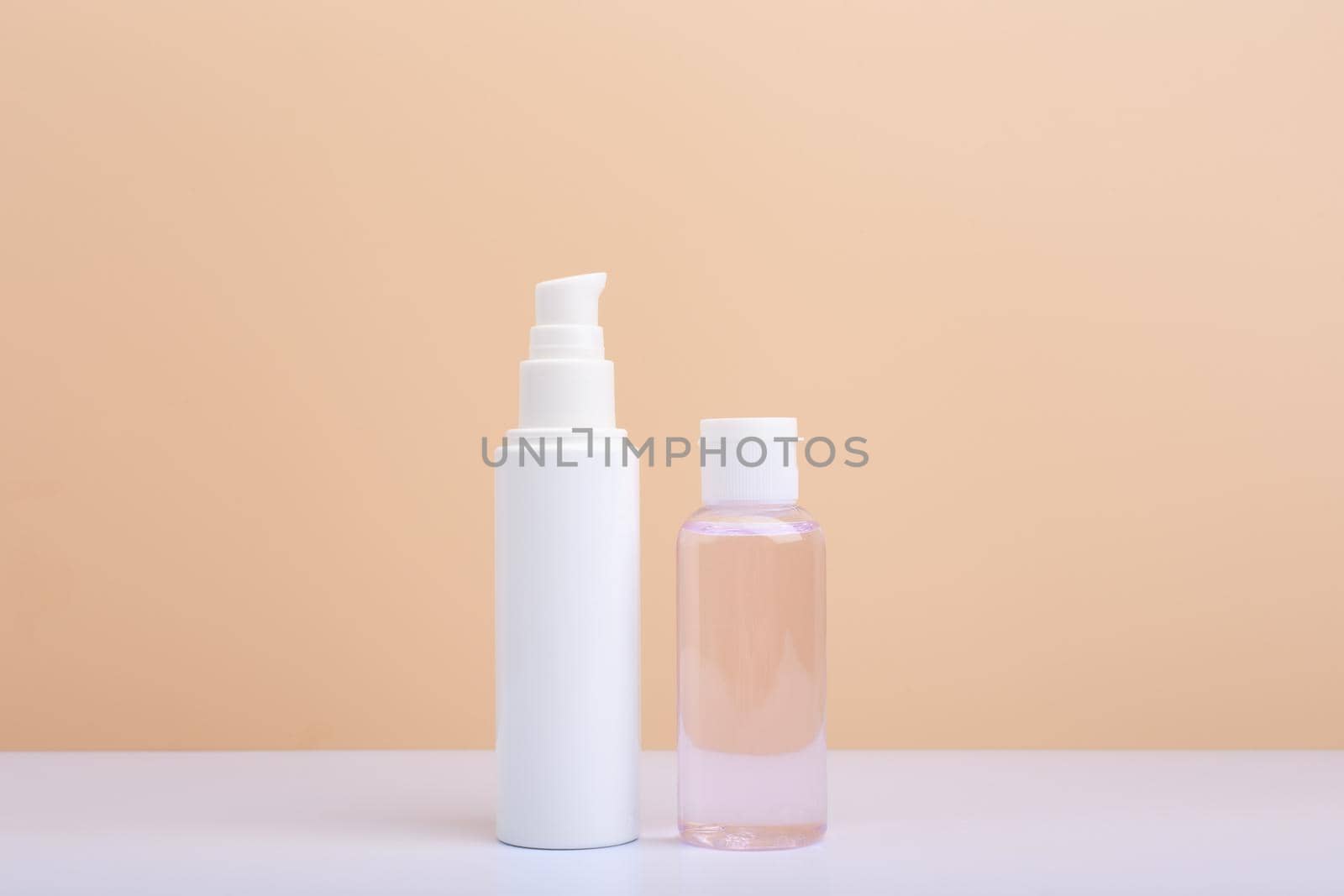 Face cream in white tube and skin lotion in transparent bottle against light beige background with copy space. Concept of beauty products and cosmetics with natural organic ingredients