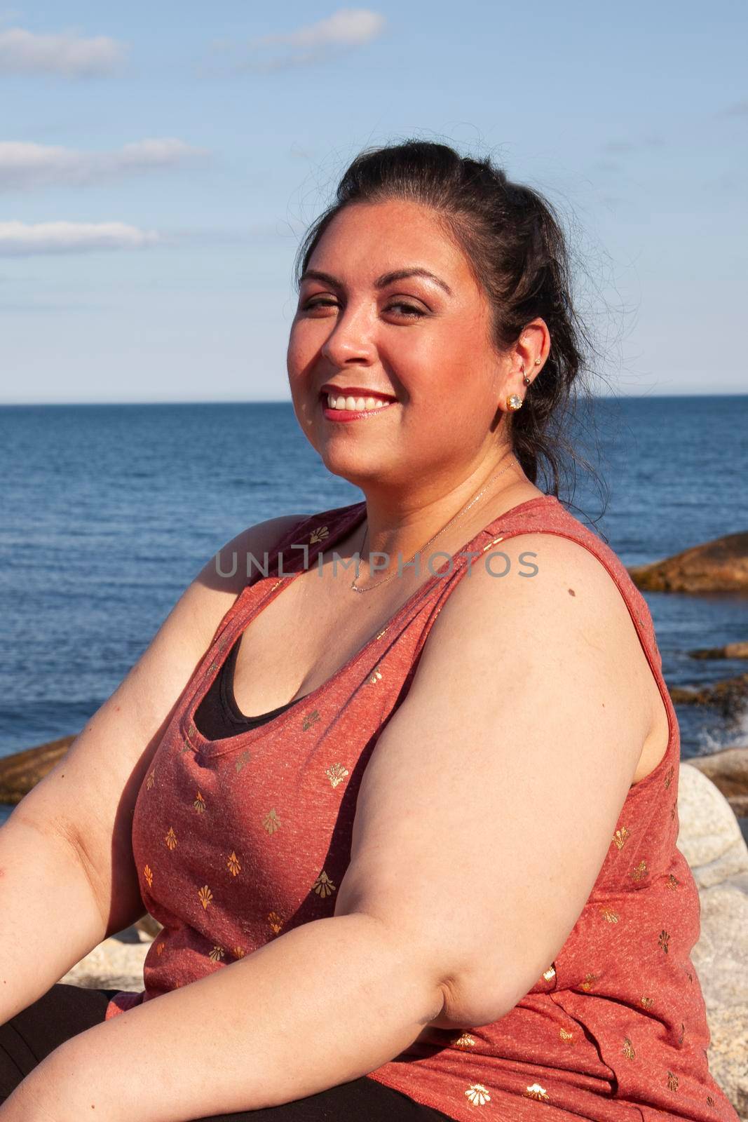 fresh real woman outdoors smiling while sitting beside the ocean in the sunshine 