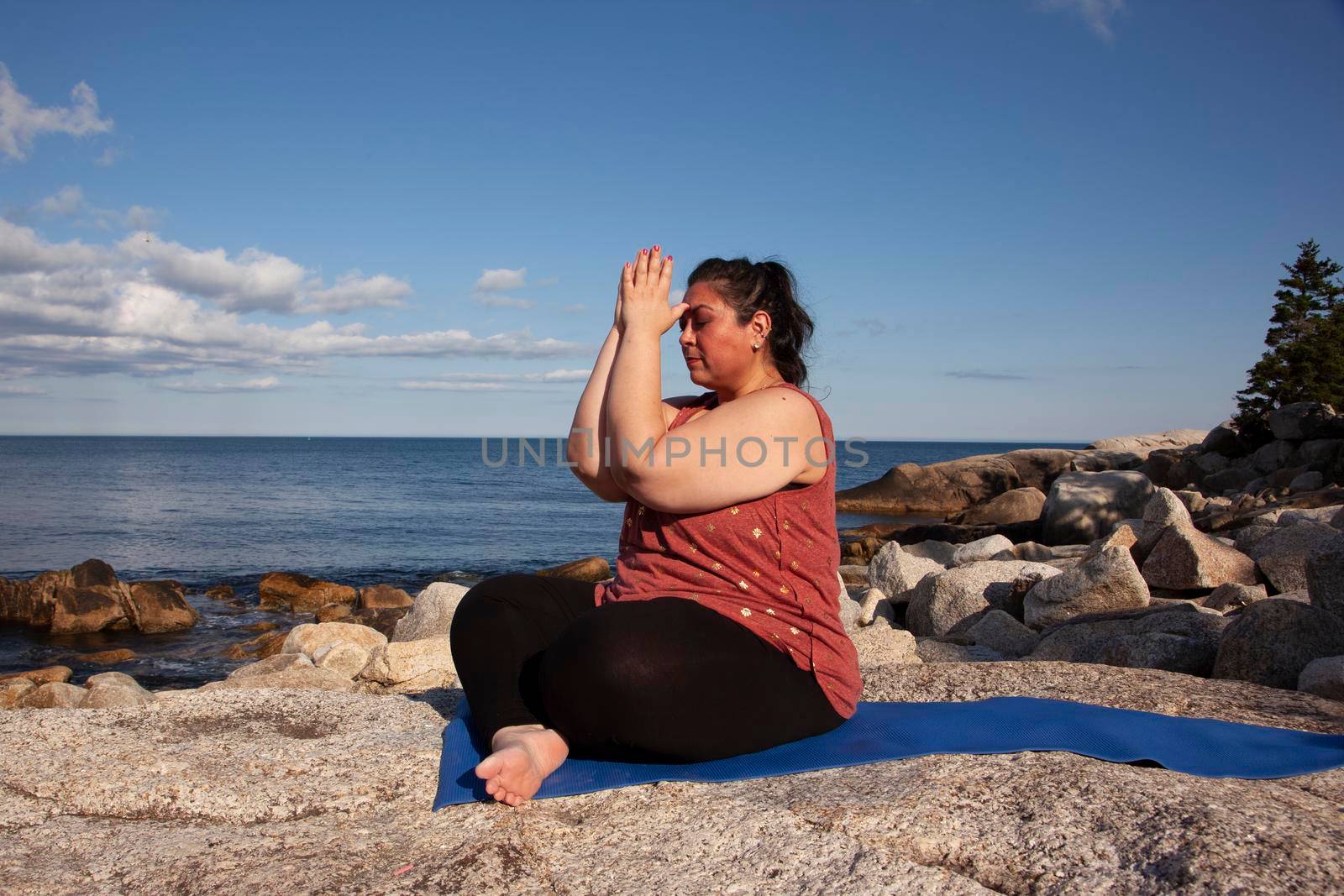 beautiful woman sitting by the ocean with hands at third eye during meditation or yoga 