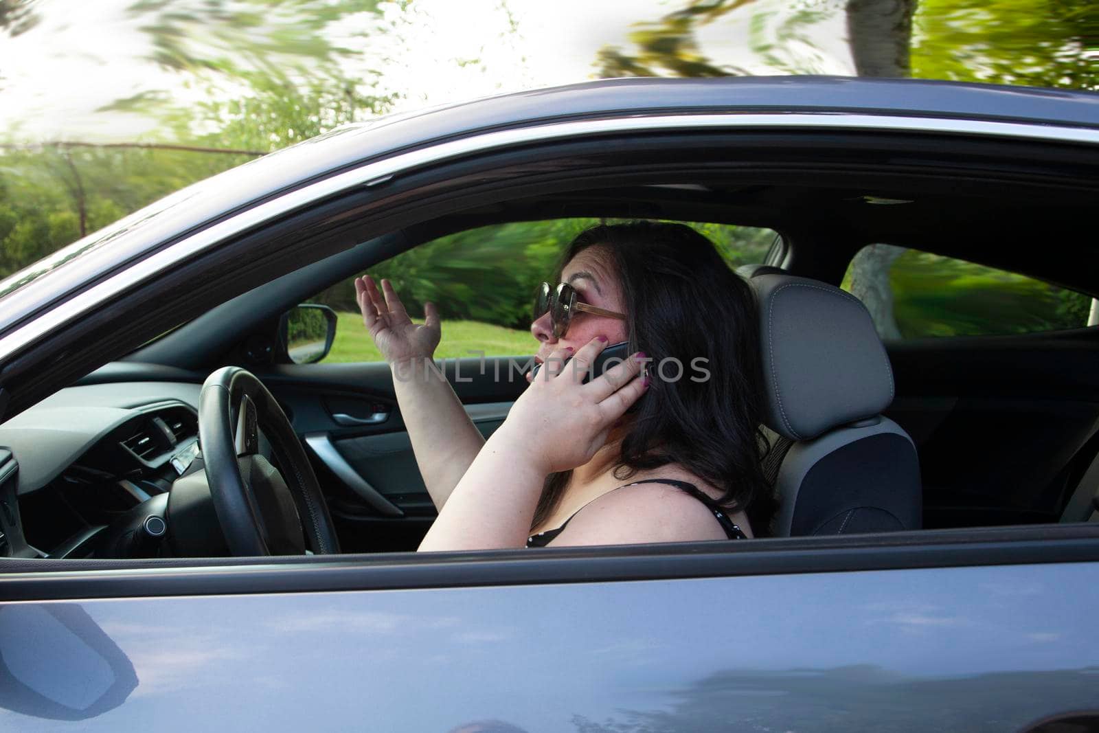 woman is distracted talking on her mobile phone while driving with no hands on the steering column 