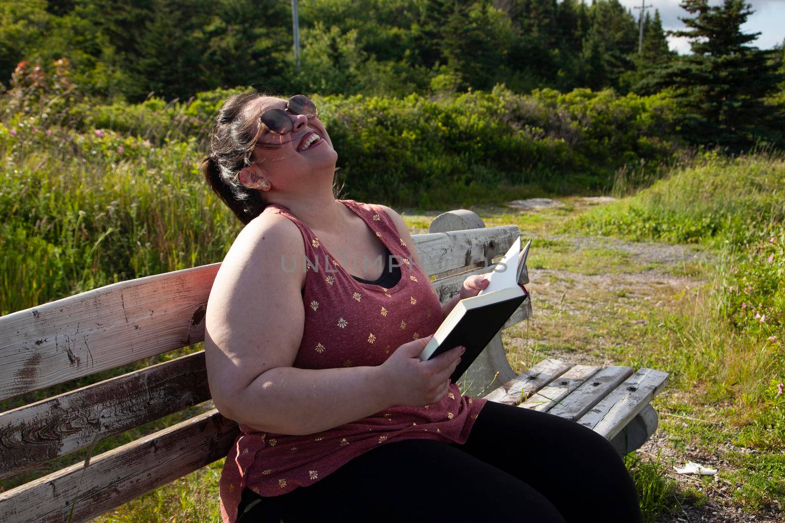 Woman chuckles while reading her book outside on a park bench 