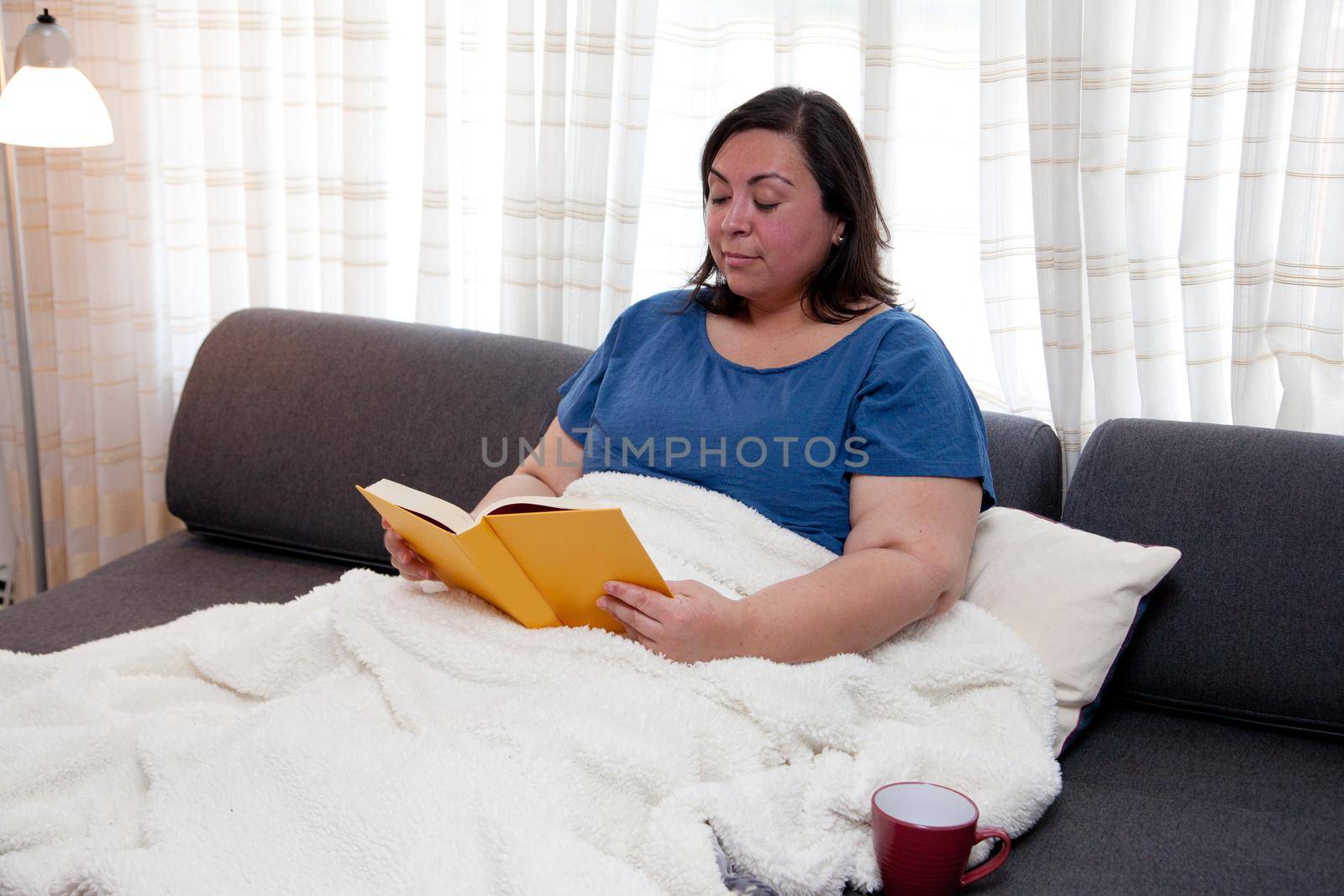 Real woman relaxing on her couch with a book and mug 