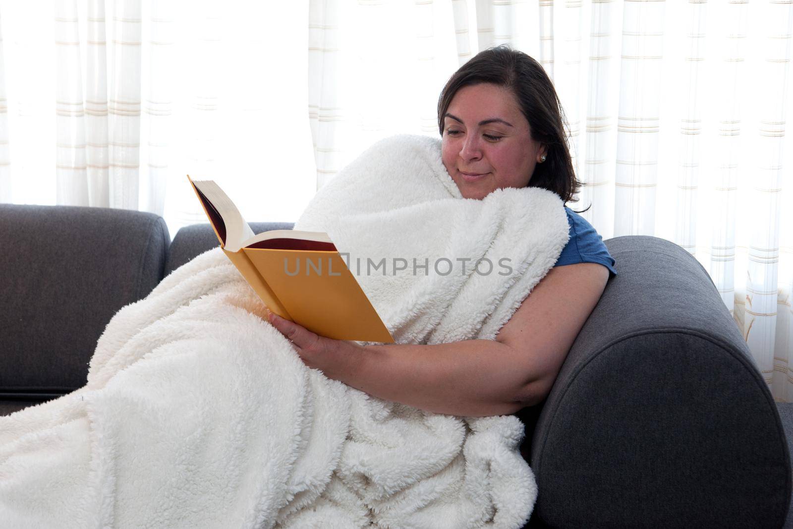Woman smiles as she is comfortable at home with a blanket and a compelling story