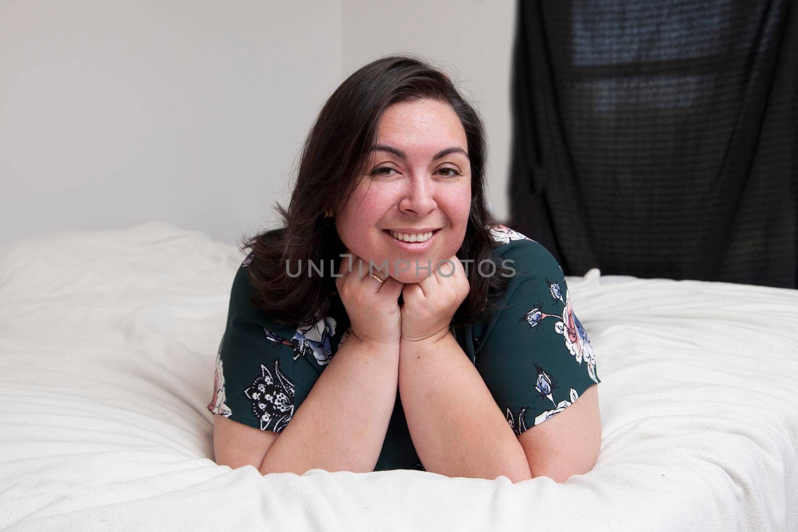 A relaxed happy woman lays on her bed at home looking at the camera in a portrait