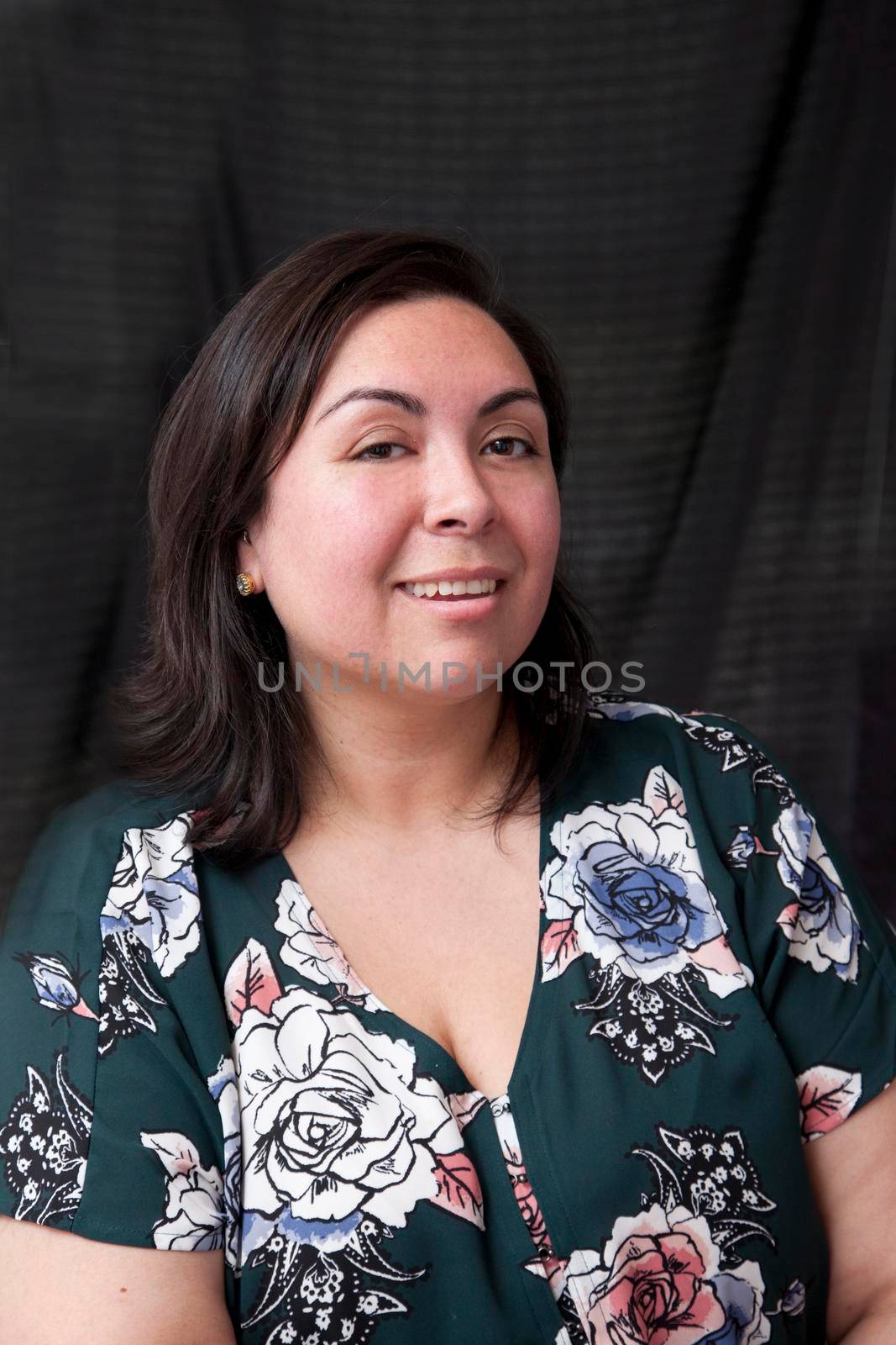 Against a black curtain, a sexy smiling hispanic woman looks at you