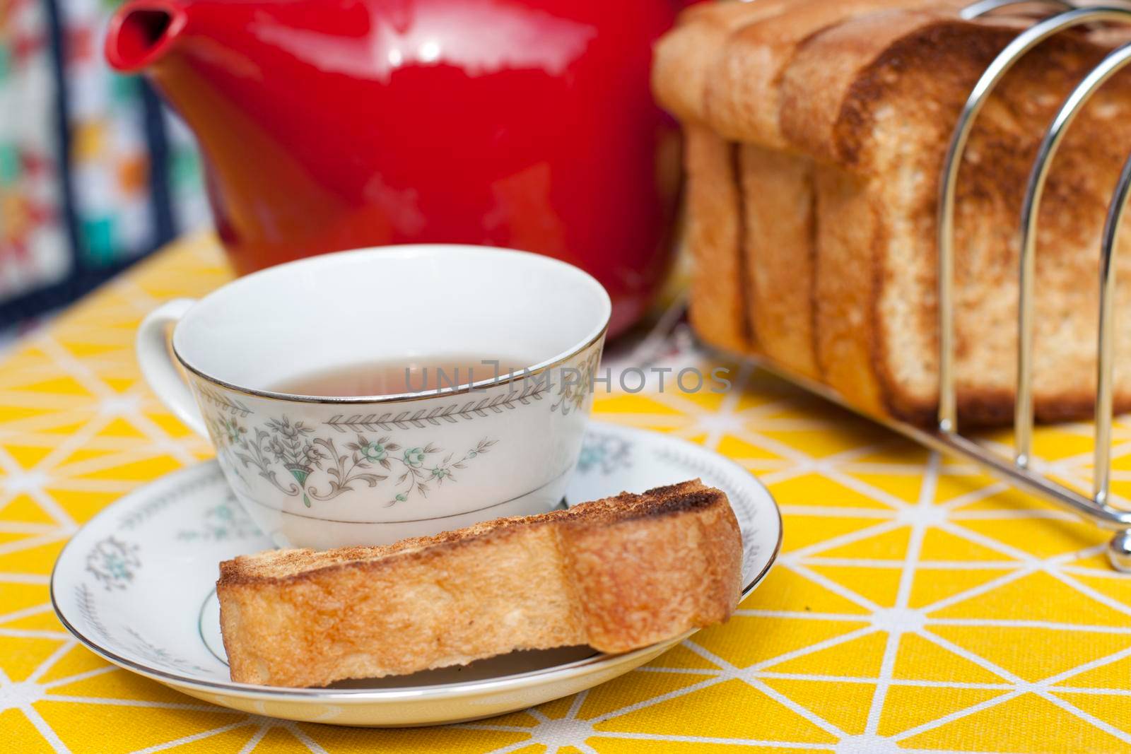 A red teapot with a cup and saucer and toasted bread