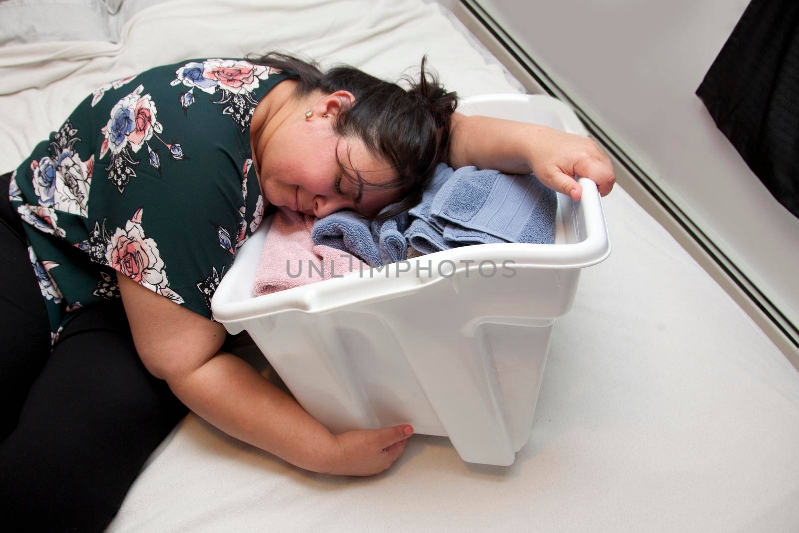 Latina woman has fallen asleep in a basket with several colorful folded towels 