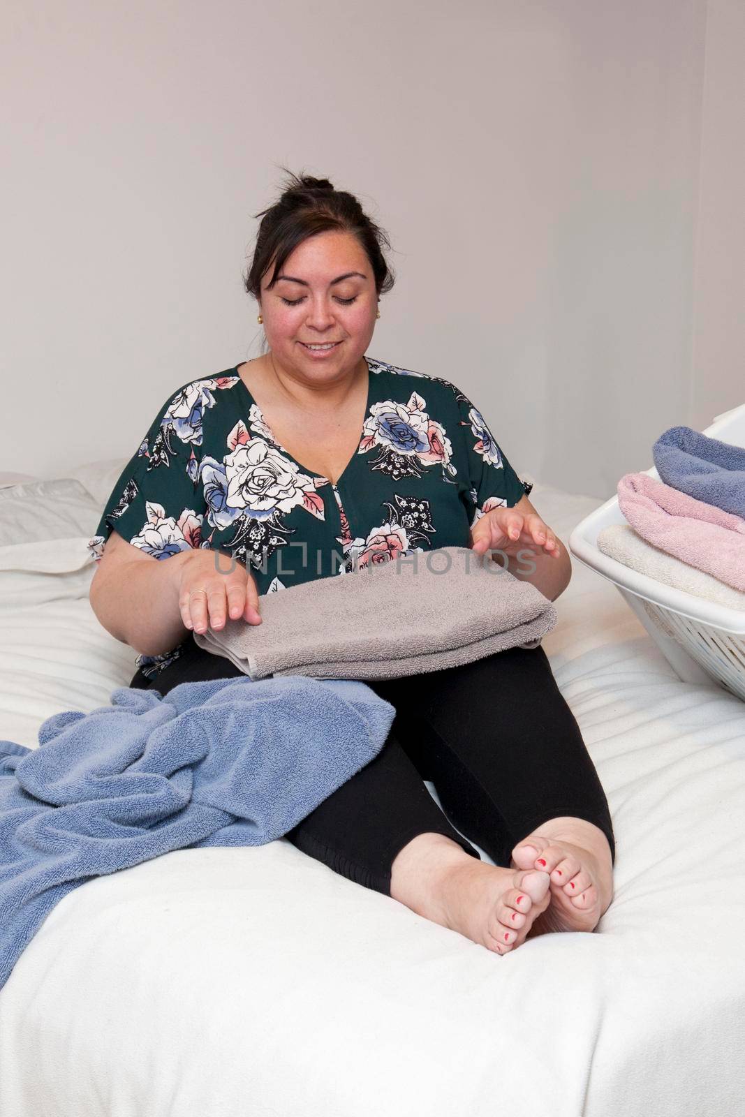 Woman folding fluffy towels on the bed at home smiles down into her work 