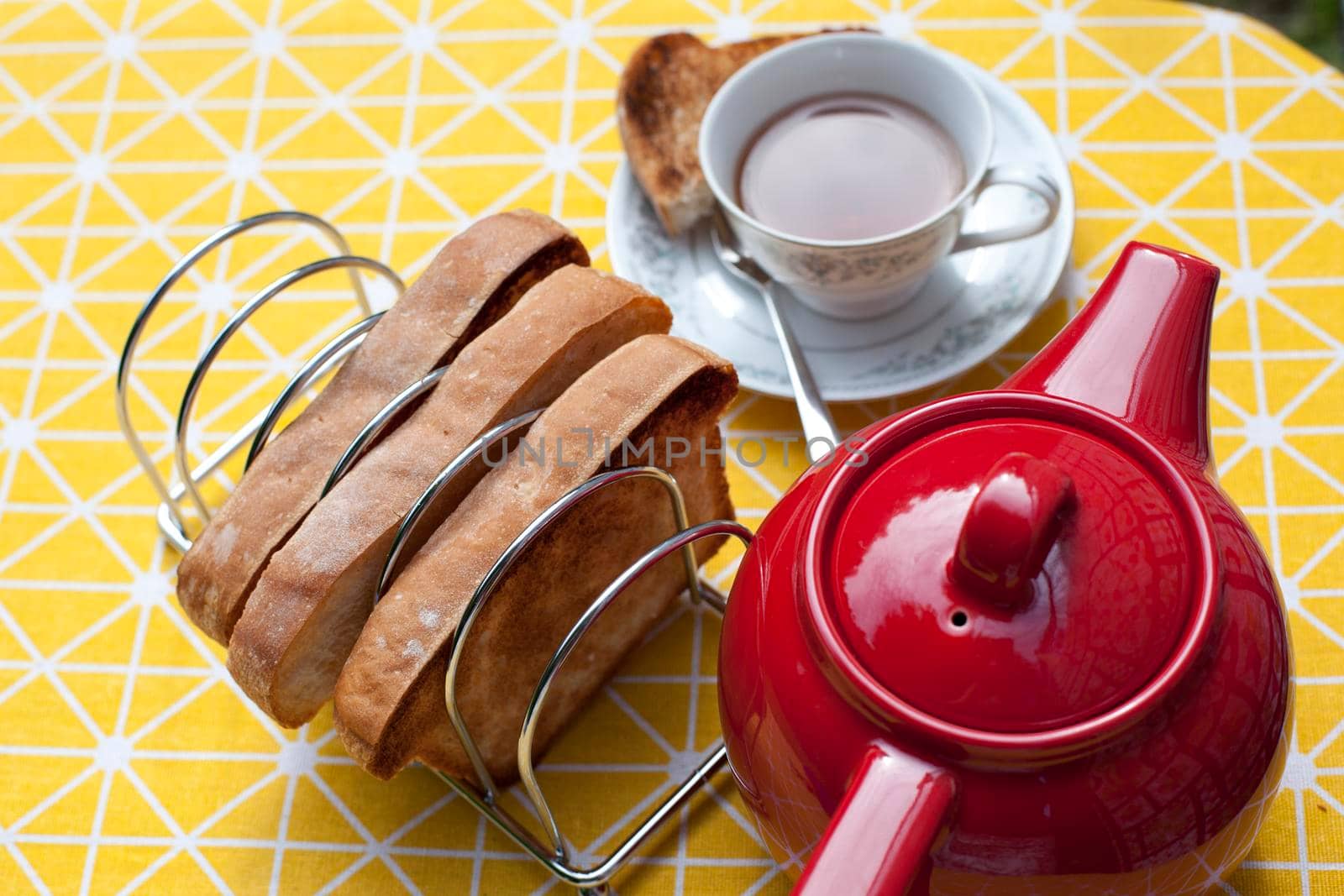 Yellow tablecloth with a red teapot and cup and saucer with toast