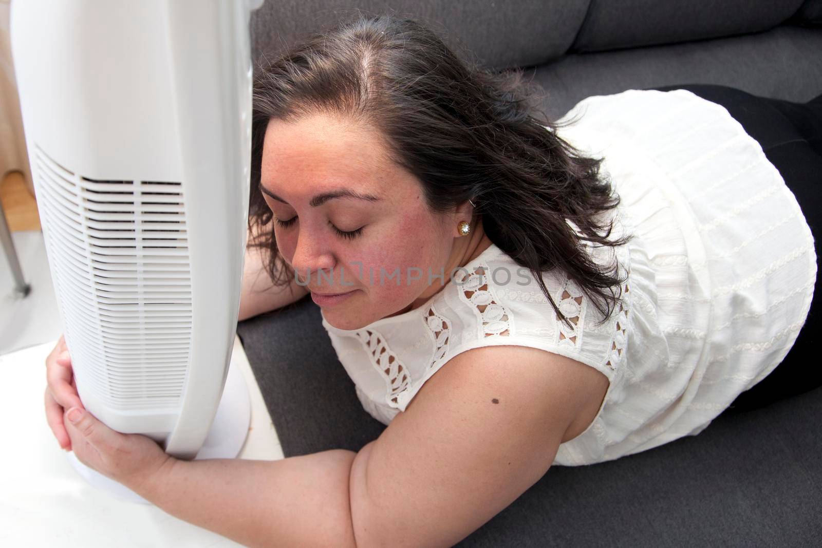 Person suffering from the heat wraps her arms around her fan at home 