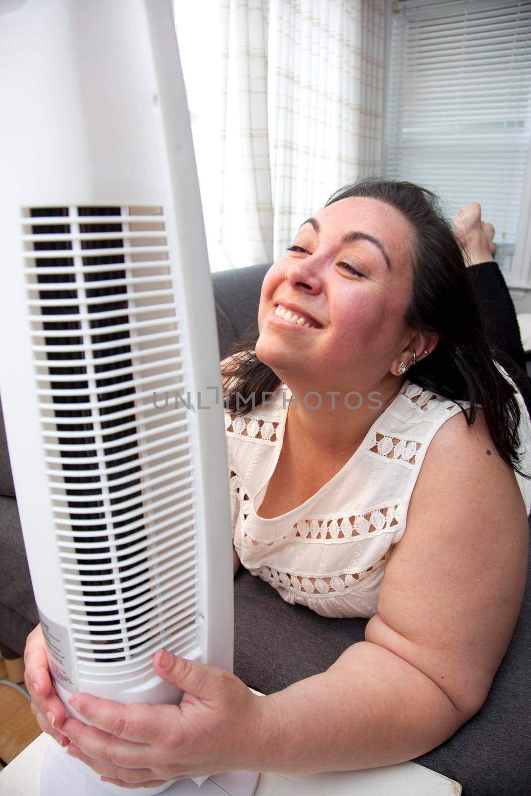 Woman hugs her fan that keeps her cool in the middle of the summer heat 