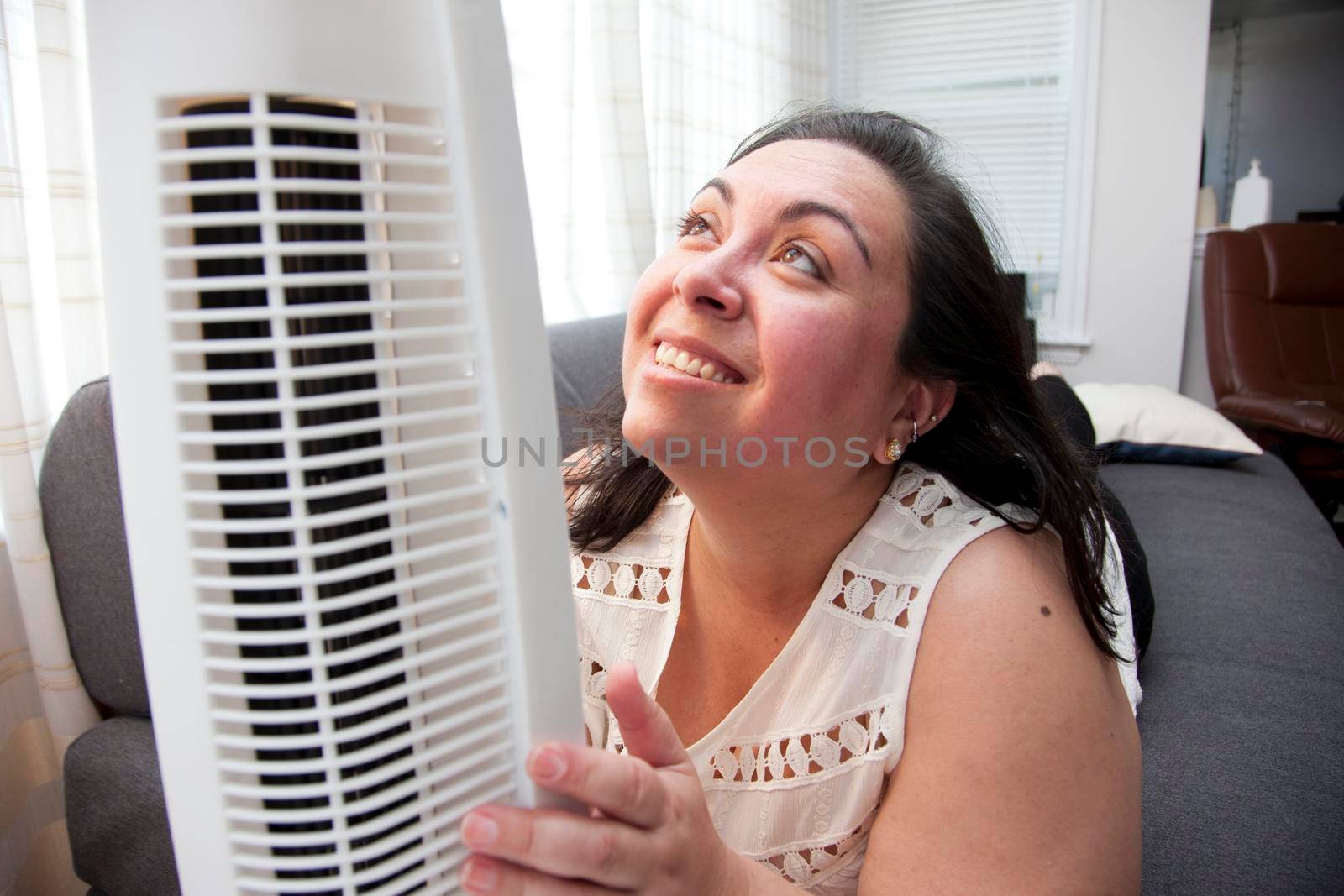 A woman who is warm in the heat hugs and looks up lovingly at her air fan 