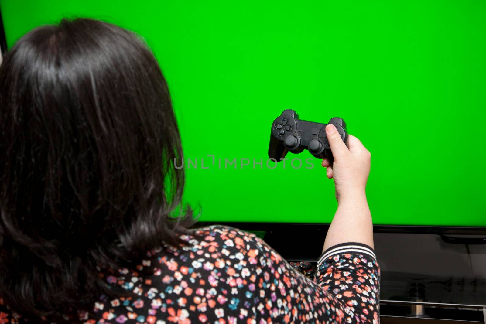 against a green screen, a woman holds a video game controller with one hand 