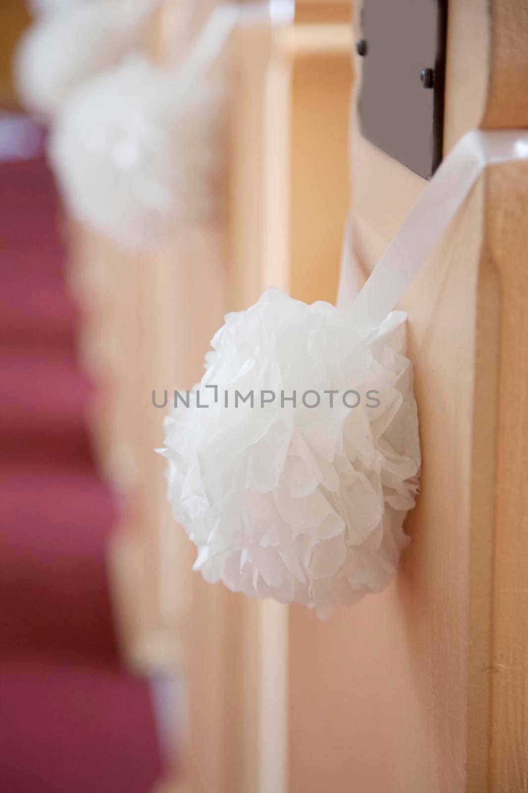 Wedding decoration in a church with a white hanging ball of flowers hung by a ribbon and blank pew plaque