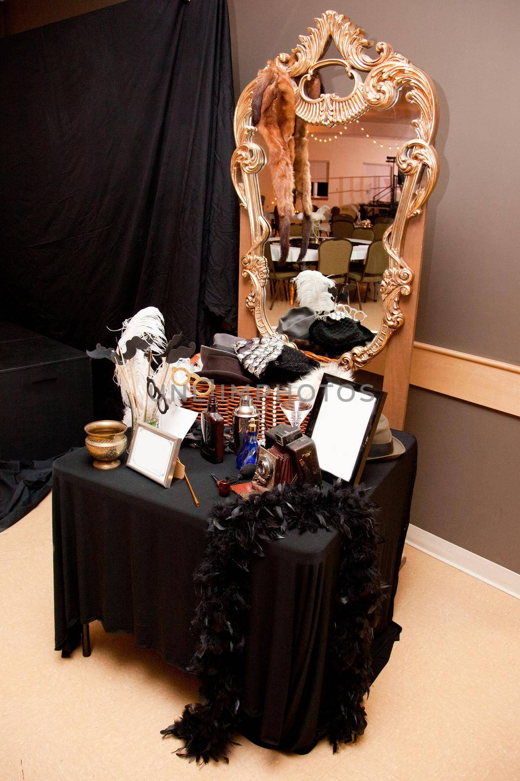 Gold mirror with photobooth props from the 1920s including feather boas, an old camera and hats 