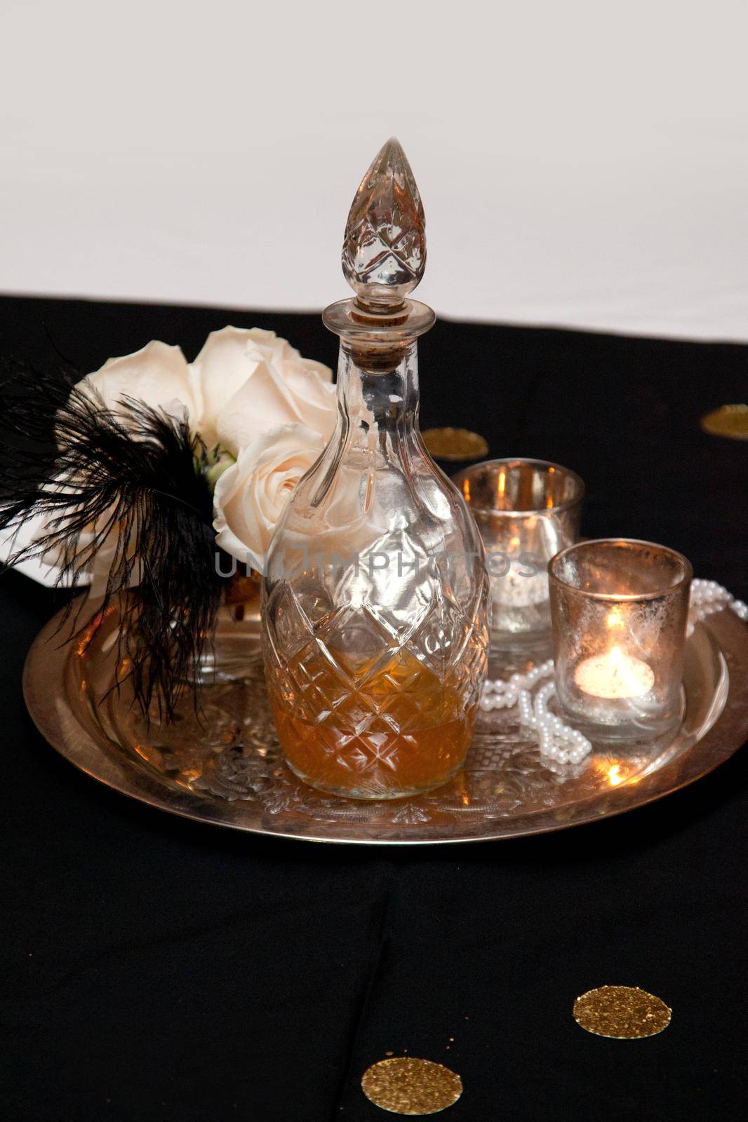Old fashioned glass liquor decanter with candles, flowers and feather decorations on top of a table 