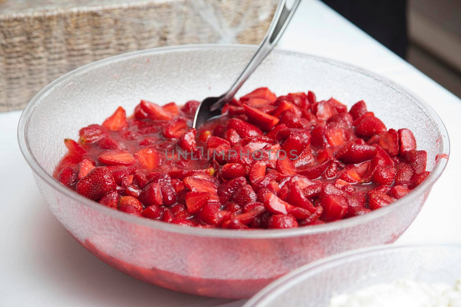 A large plastic dish of mashed strawberries with a spoon ready for dessert