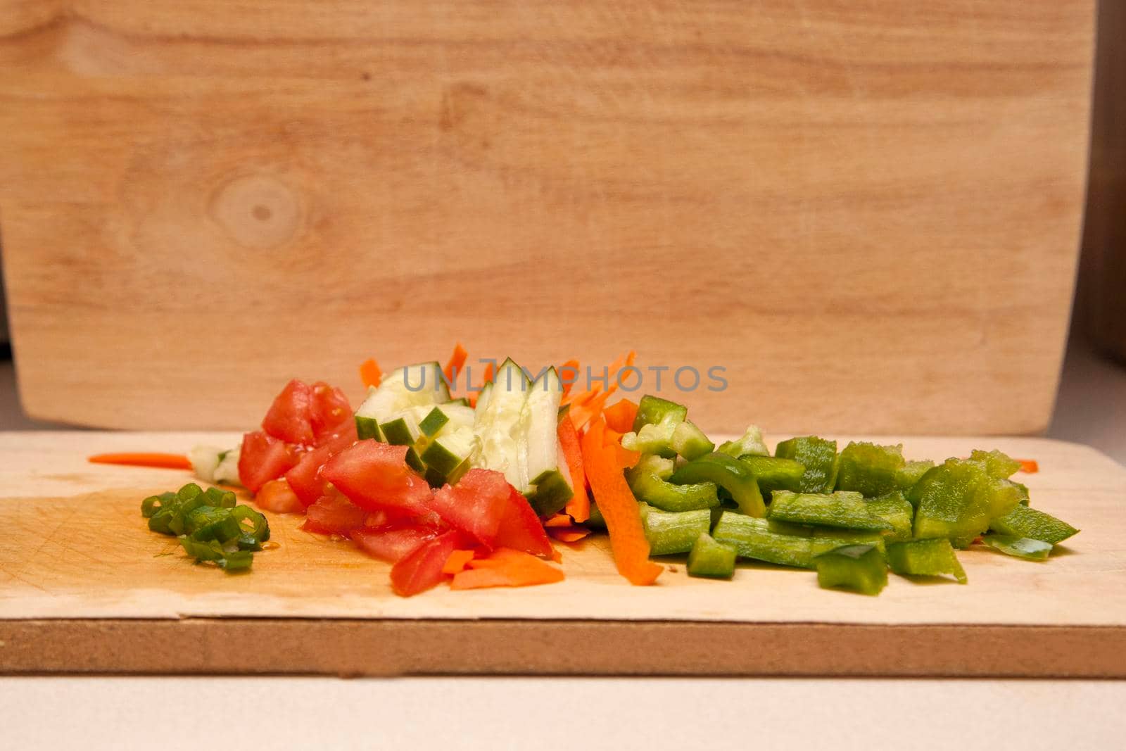 cut up green onion, cucumber, tomato, green pepper on a wooden cutting board 