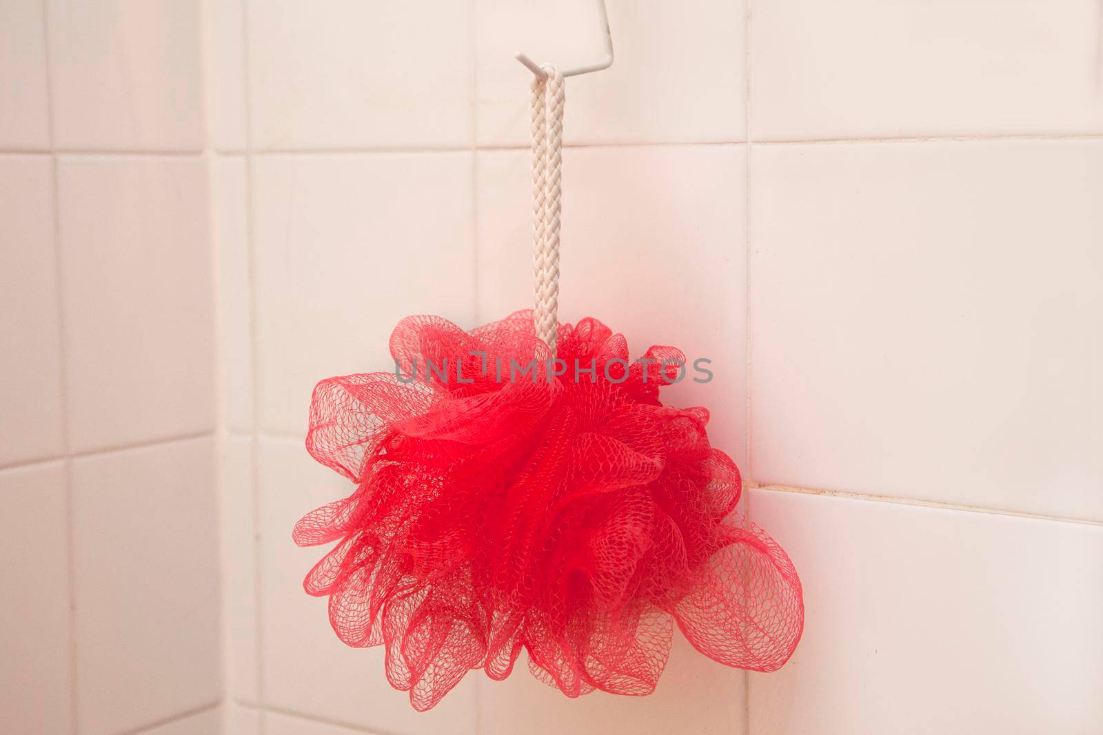 A red mesh scrubbing loofah hangs from a hook in a shower or bath