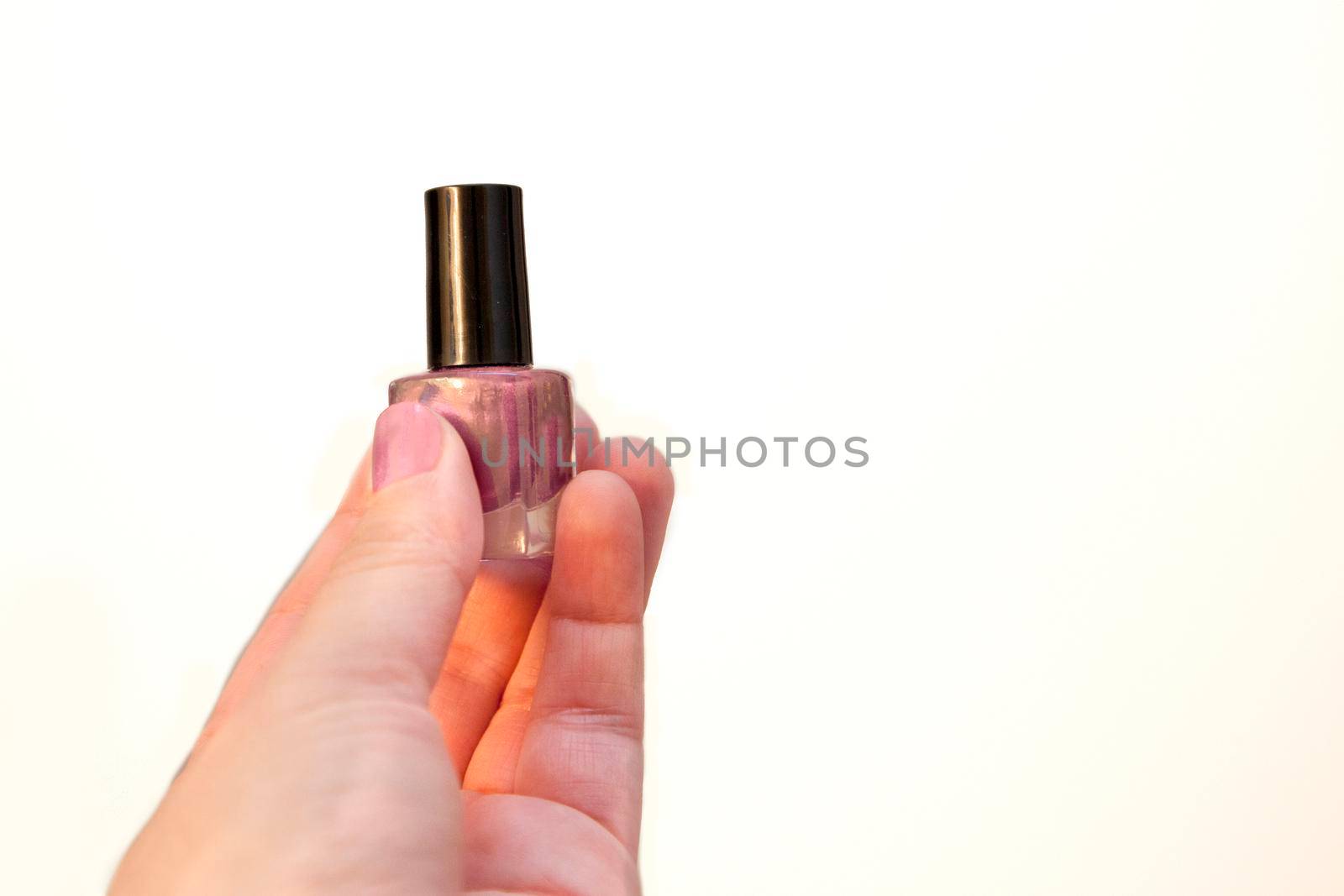 A hand holding a glass bottle with pink shiny nail polish with a black cap against white copy space