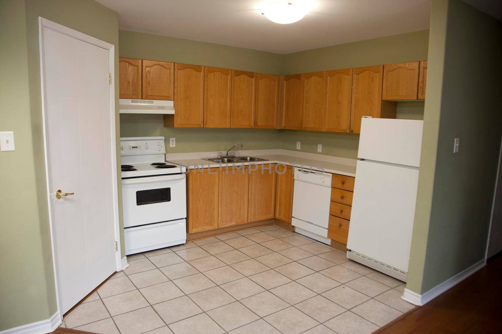 Looking into a small empty kitchen with stove, fridge and cupboards