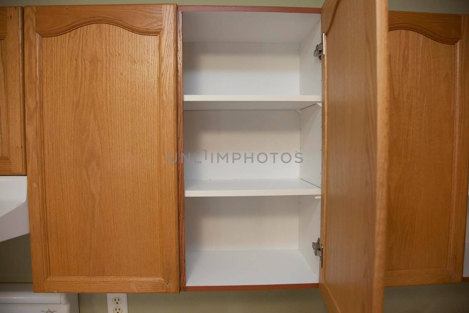 Kitchen cupboard with wooden doors and open to see empty shelves