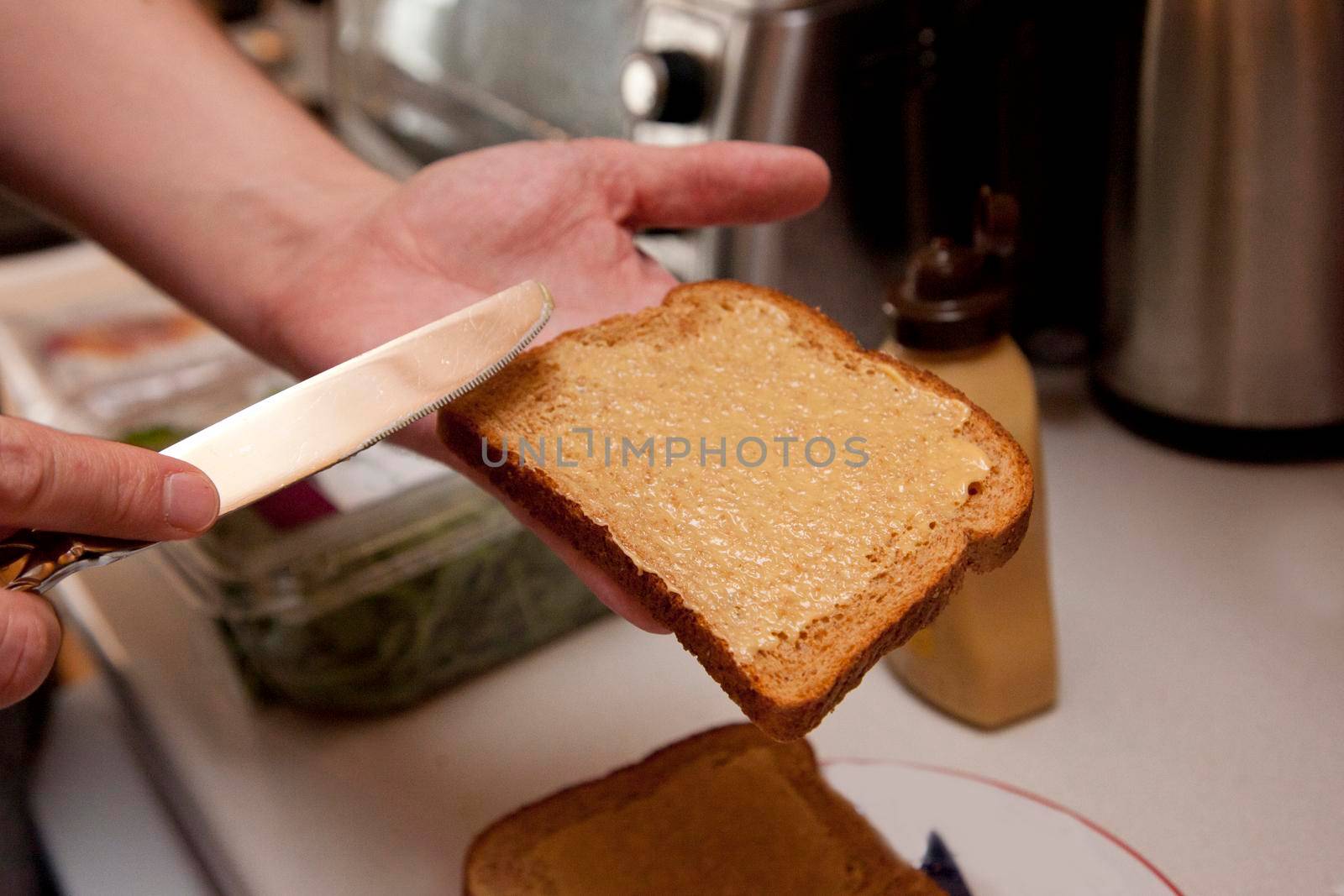  hand spreading mustard with a knife onto a piece of bread to make a sandwich