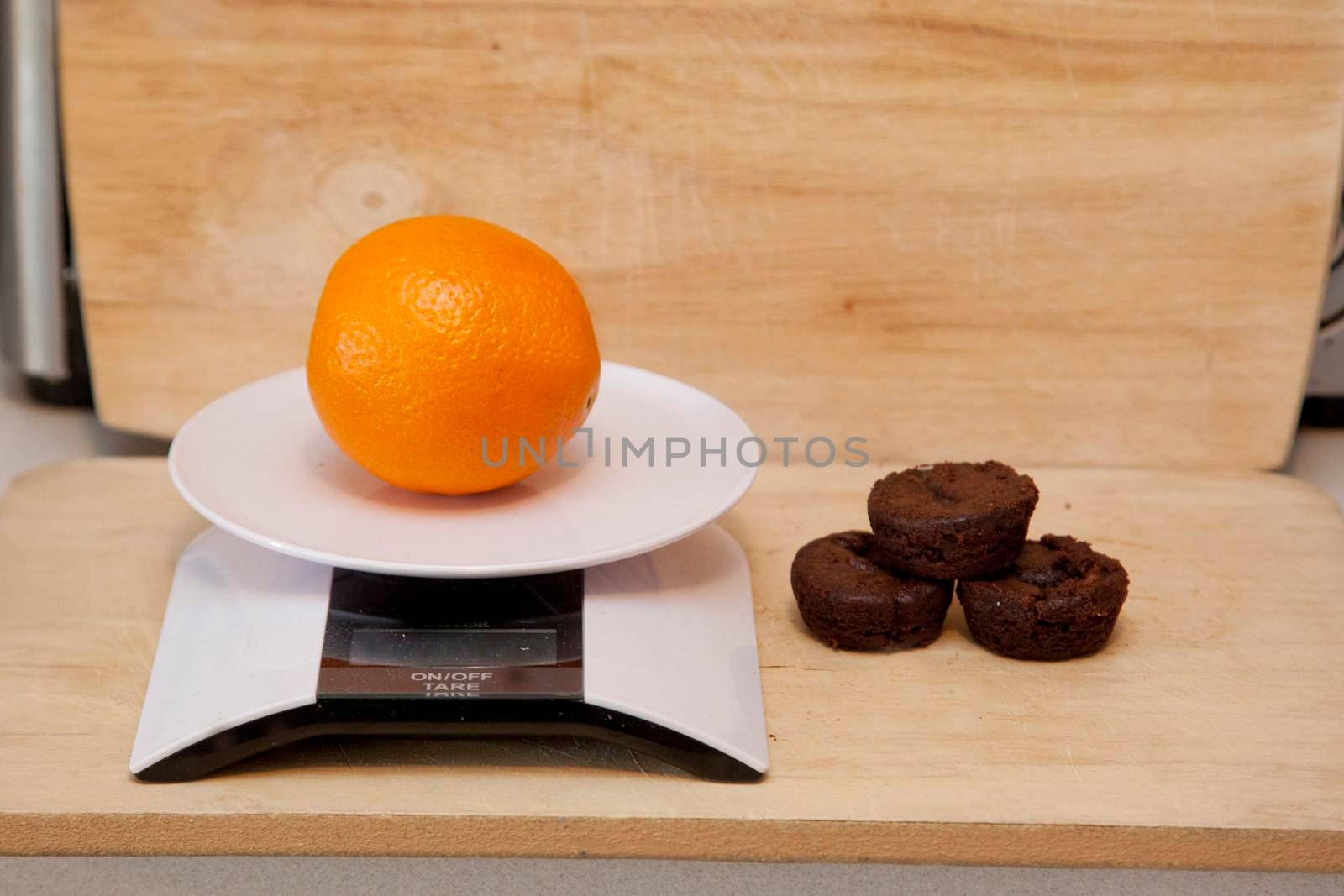 An orange on a digital scale beside a pile of brownies 