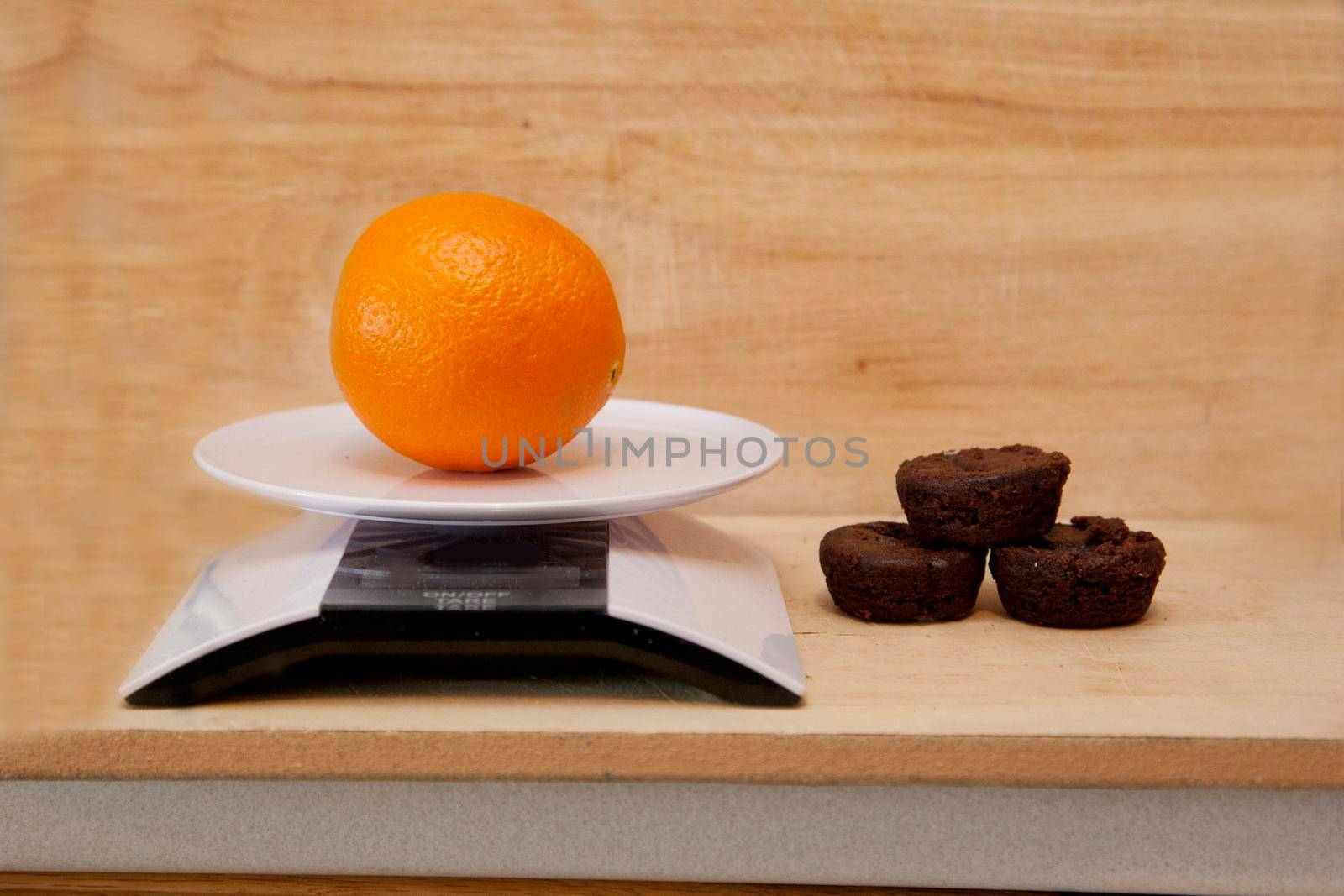  weighting an orange beside a pile of small brownies for choosing dessert
