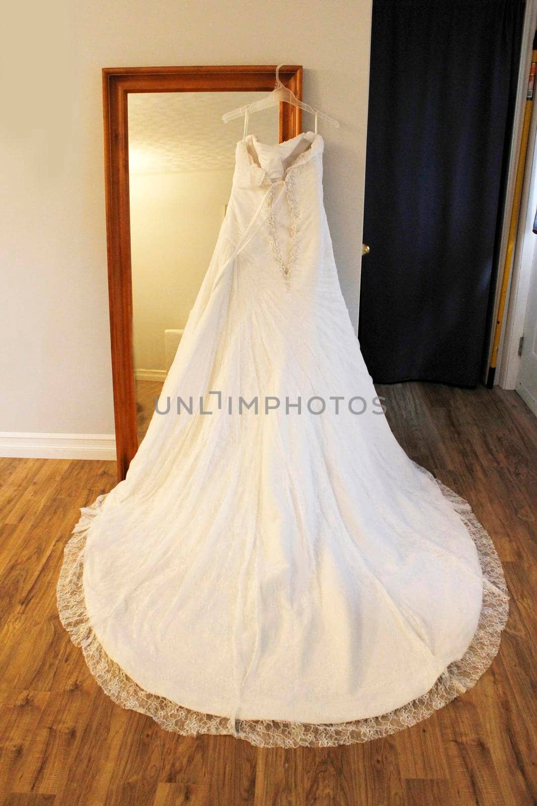 Gorgeous back view of a beautiful lace wedding dress with a round lovely train hung on a mirror
