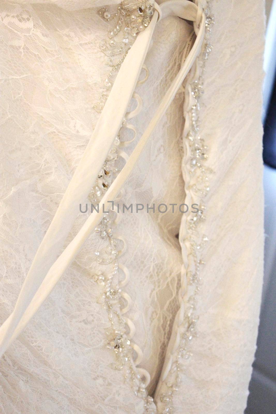 The back side of a beautiful ivory colored wedding gown being laced up with a long ribbon 