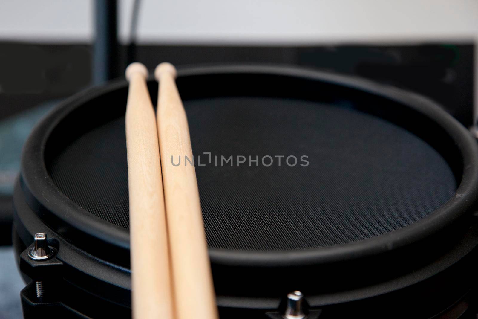 Black electronic drum with two wooden sticks resting with copy space to the side 