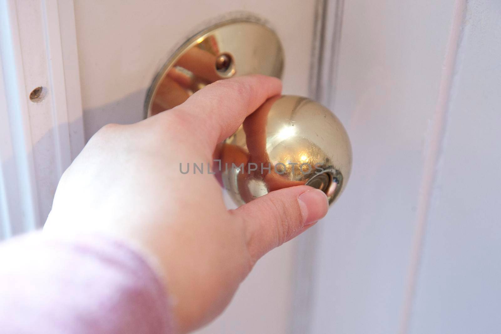  Hand on a gold door knob with thumb pushing the button to lock the door 