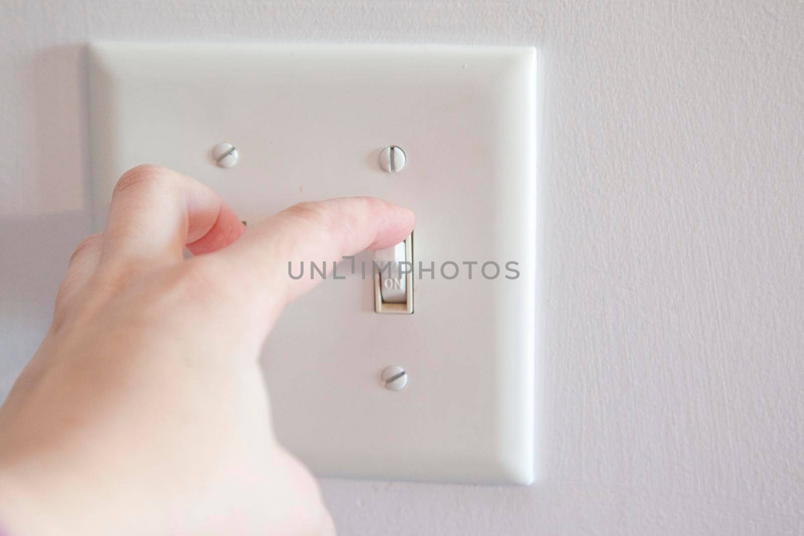 Hand about to turn a light switch from the on position to off 